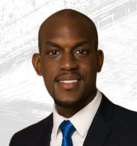 Jamell Henderson’s professional headshot, smiling in a navy suit and bright blue tie against a subtle cityscape backdrop, emphasizing leadership and community engagement.