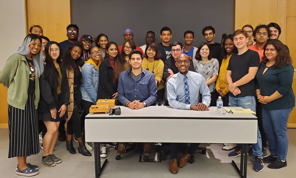 Jamell Henderson seated at center posing with a diverse group of college students during a youth engagement event, highlighting civic leadership and community outreach.